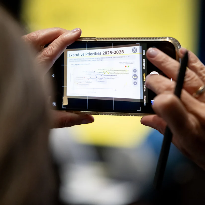 A person holds a smartphone and stylus, taking a photo of a screen displaying "Executive Priorities 2025–2026" and a list of bullet points.