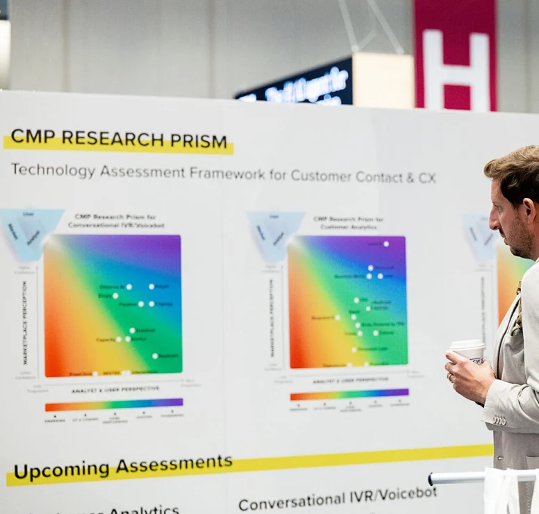 A man in a light suit holding a coffee cup stands beside a presentation board displaying colorful research diagrams and text about a technology assessment framework.