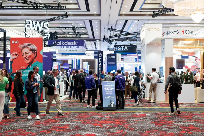 People walk and interact at a busy technology conference expo hall with various company booths and banners visible.