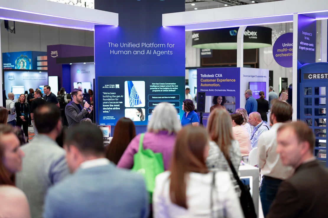 A group of people attends a technology expo booth with digital displays and a sign reading "The Unified Platform for Human and AI Agents.