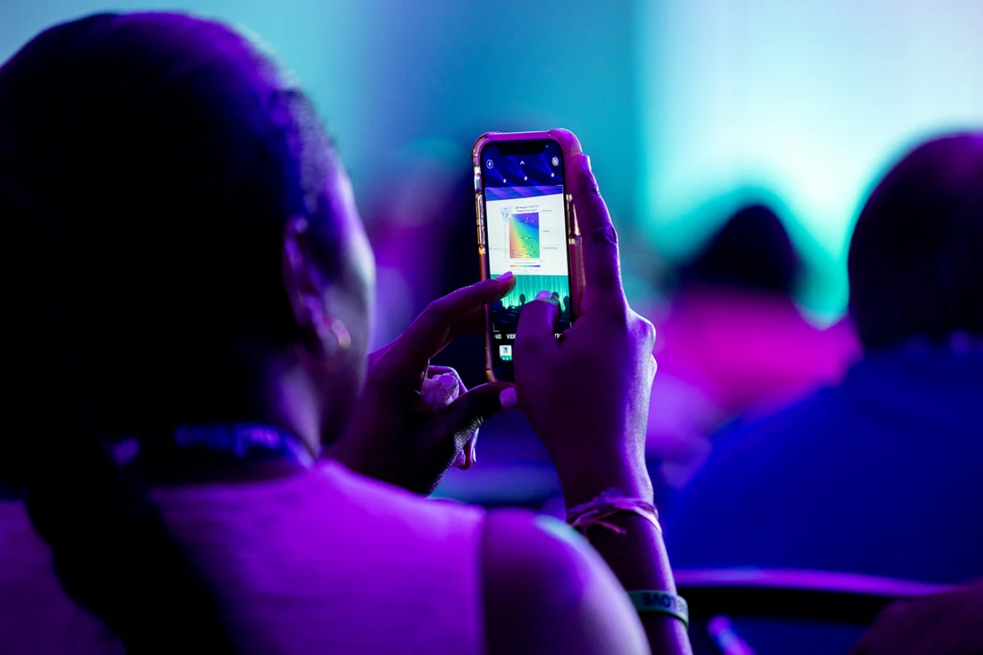 A person holds up a smartphone to take a photo of a projected chart or presentation screen during an event or conference.