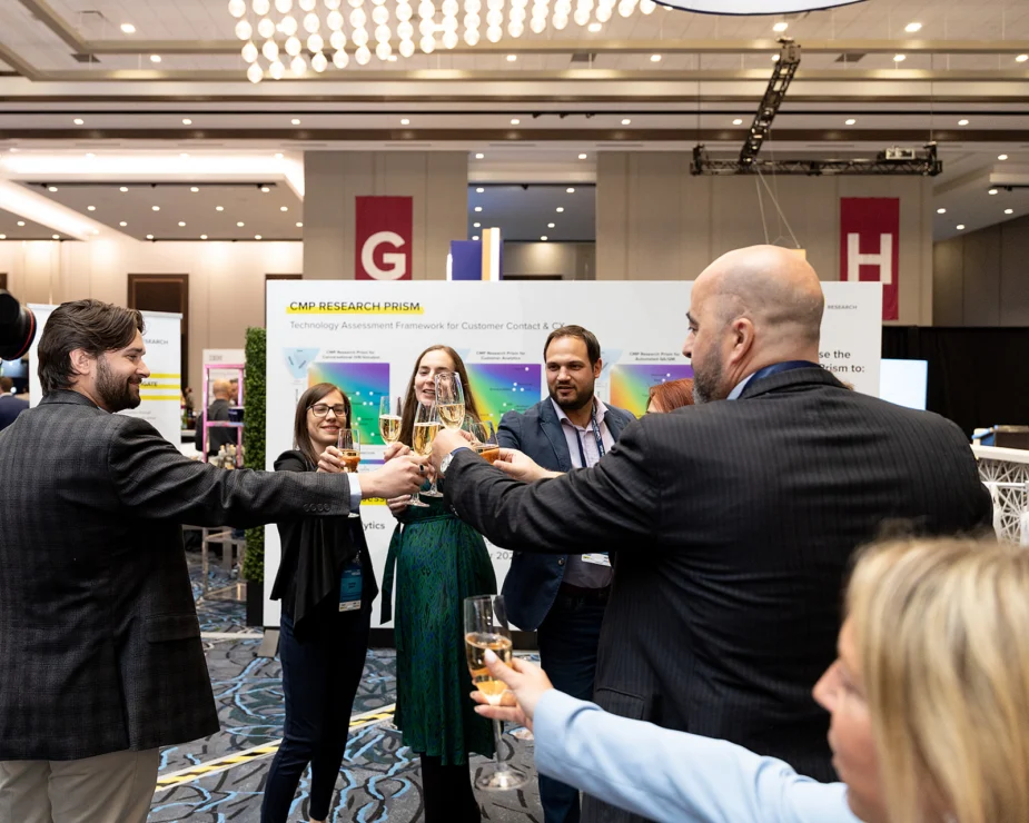 A group of people wearing business attire clink glasses in a toast at a conference or event, standing in front of a research display booth.