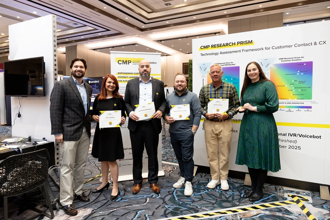 Six people stand indoors at a conference, holding certificates in front of a CMP Research PRISM display about customer contact and CX.