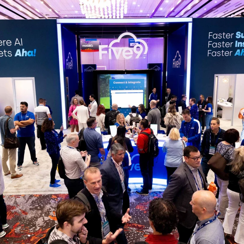 A busy convention booth for Five9 with people networking and digital displays promoting AI, support, and insights messaging.