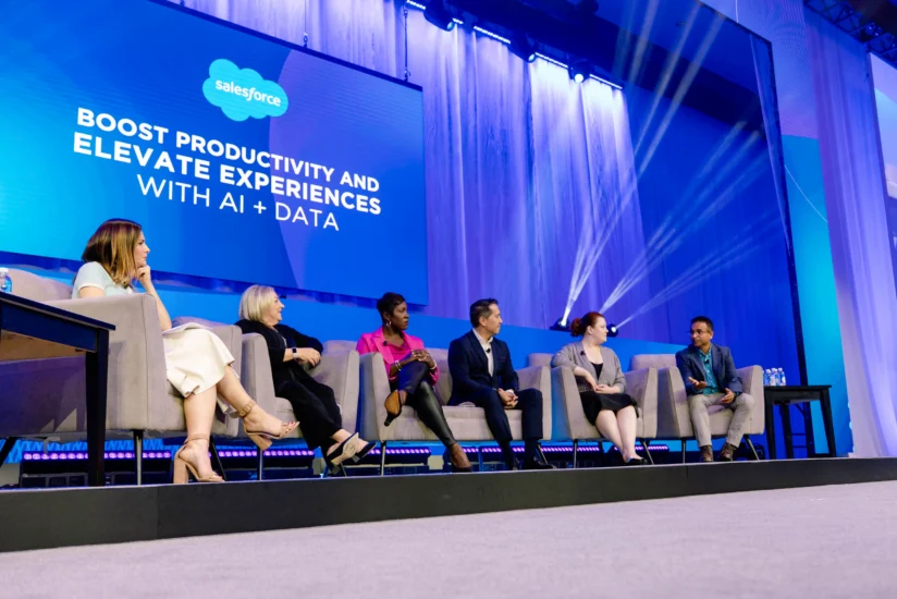 Six panelists sit on stage discussing AI and data, with a screen behind them displaying "Boost productivity and elevate experiences with AI + Data" at a Salesforce event.