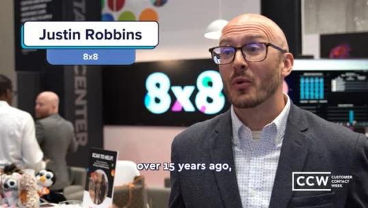 A man in a suit and glasses speaks at a trade show booth with the name "Justin Robbins" and "8x8" displayed on screen. The CCW Customer Contact Week logo is visible.