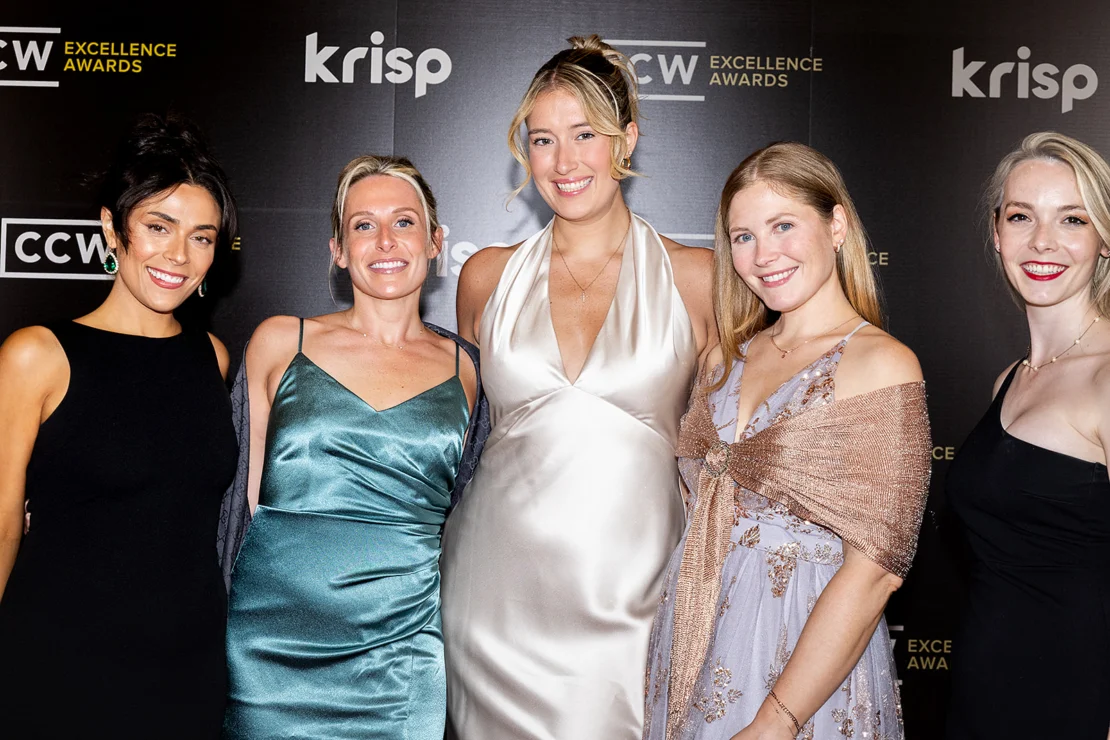 Five women dressed in formal attire stand together and smile in front of a step-and-repeat banner featuring "CCW Excellence Awards" and "krisp" logos.