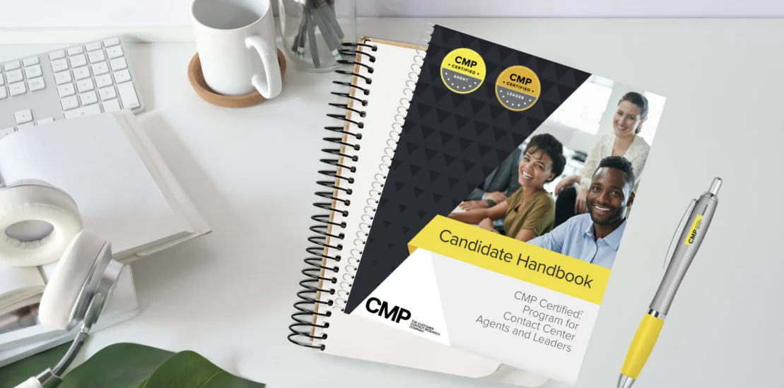A spiral-bound Candidate Handbook for the CMP Certified Program rests on a desk beside a keyboard, headphones, a plant, and a pen.