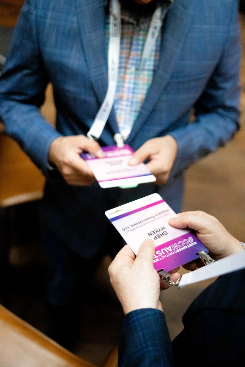 Two people in business attire hold and look at conference name badges while standing indoors.