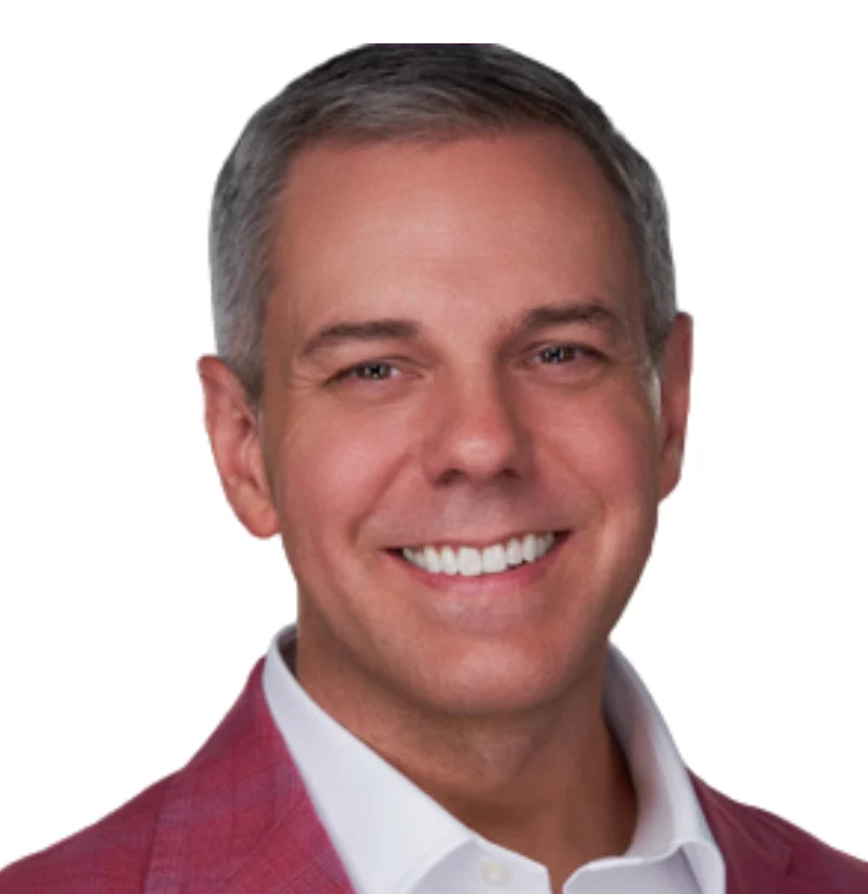 Smiling man wearing a pink blazer and white collared shirt, posing against a white background.