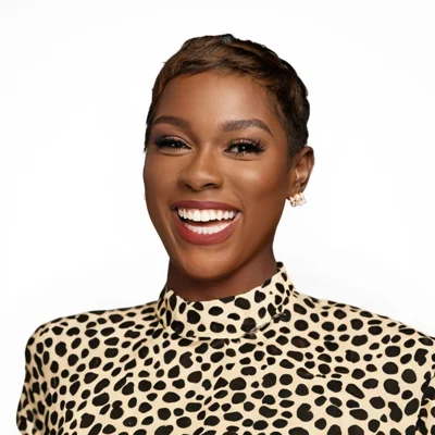 A person with short hair smiles, wearing a high-neck, black and white animal print top and stud earrings against a plain white background.