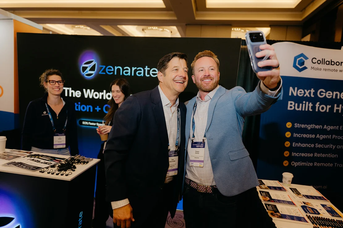 Two men pose for a selfie at a conference booth, while two women stand nearby. Booth displays feature "Zenarate" and "Collaborate" branding and informational materials.