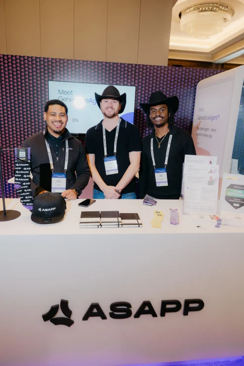 Three men wearing conference badges and black cowboy hats stand behind an ASAPP booth with promotional materials at a tech event.