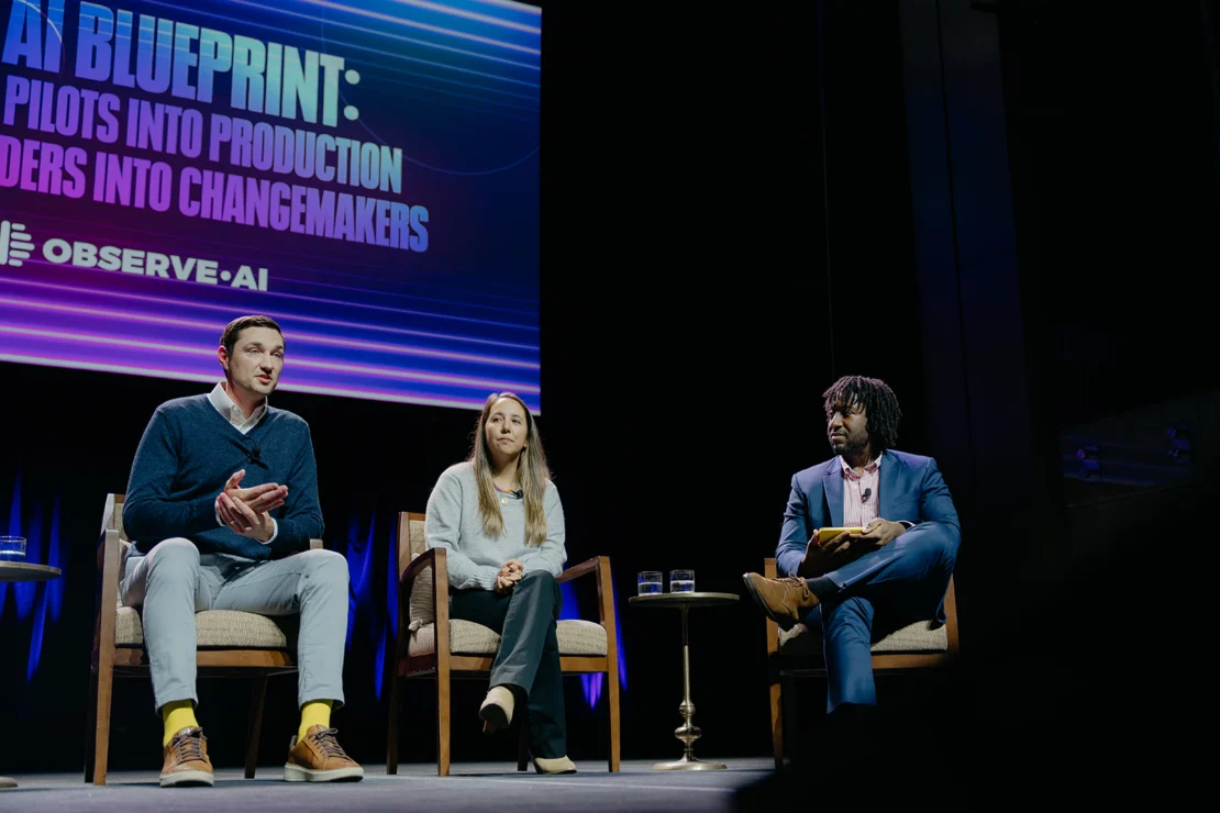 Three people sit on stage in a panel discussion. A large screen behind them displays the text “AI BLUEPRINT: PILOTS INTO PRODUCTION, LEADERS INTO CHANGEMAKERS” and the Observe.AI logo.