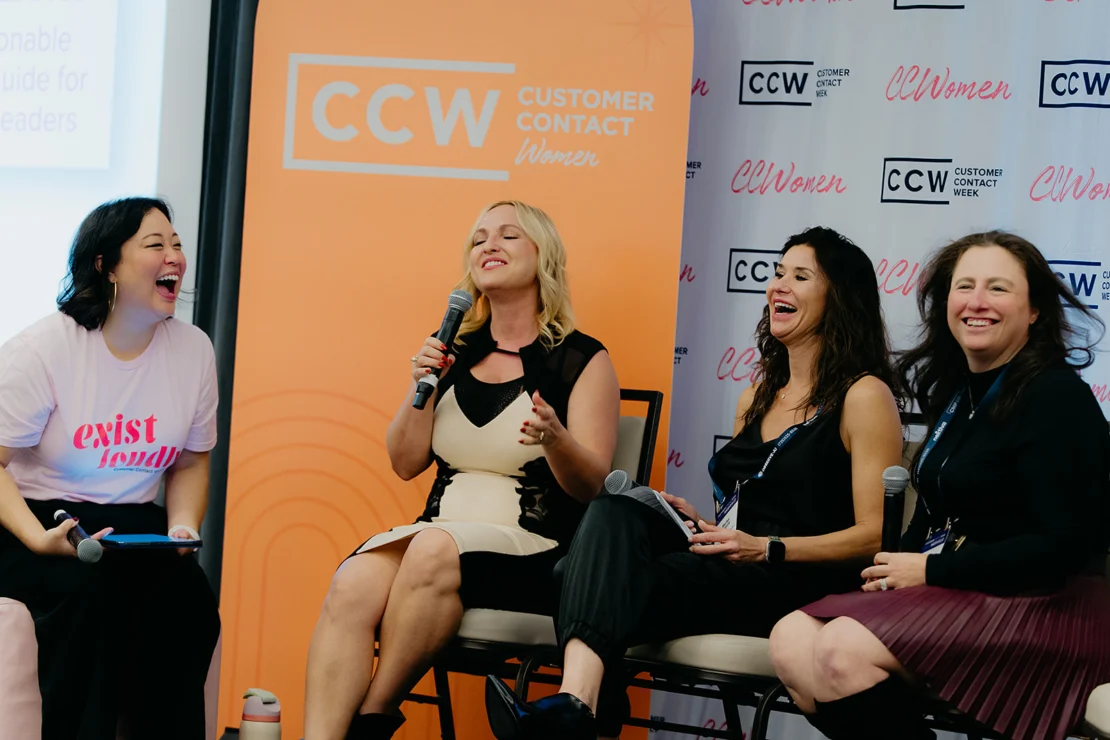 Four women sit on chairs, laughing and talking during a panel discussion at a Customer Contact Week (CCW) event. One woman holds a microphone and others have notepads and lanyards.