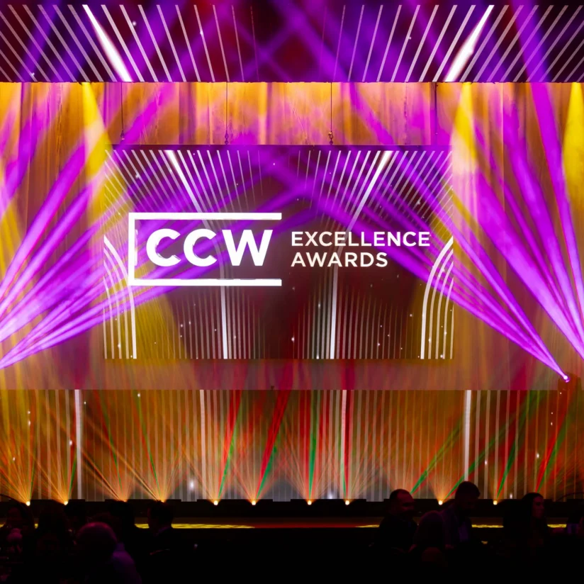 Stage set for the CCW Excellence Awards, featuring colorful purple and yellow lights with the event logo displayed on a large screen.