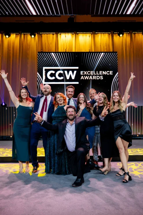 A group of people pose and smile with raised arms in front of a stage backdrop reading "CCW Excellence Awards.