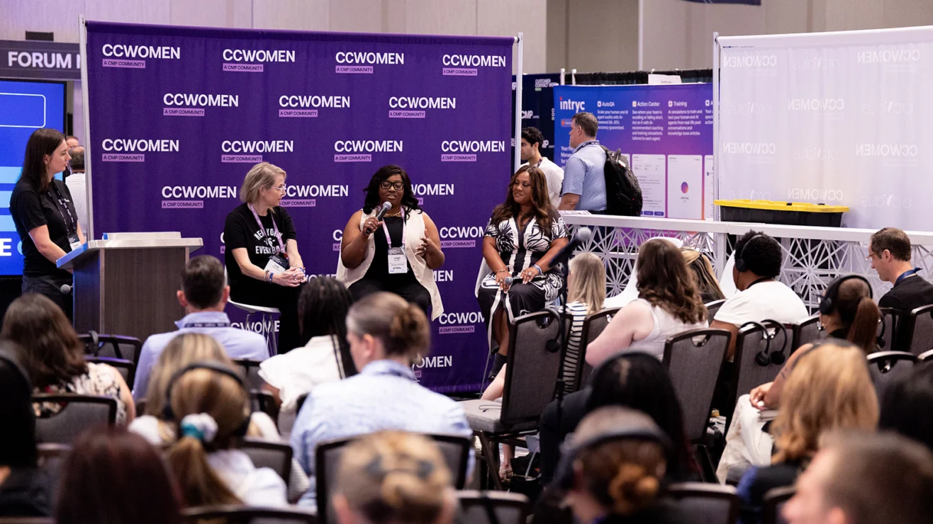 Four women sit on a panel speaking to an audience at a conference. The backdrop reads “CCWOMEN.” Attendees listen while one panelist speaks into a microphone.