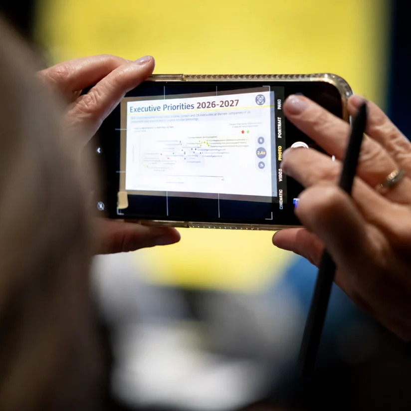 A person takes a photo of a presentation slide titled “Executive Priorities 2026-2027” with a smartphone, while holding a stylus.